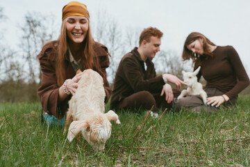 Naklejka premium Three friends enjoy a sunny day in the field with goat, goats, kid, field, outdoor, friends, people, playful, meadow, laughter as trees sway and kids explore grass, creating a warm lifestyle moment