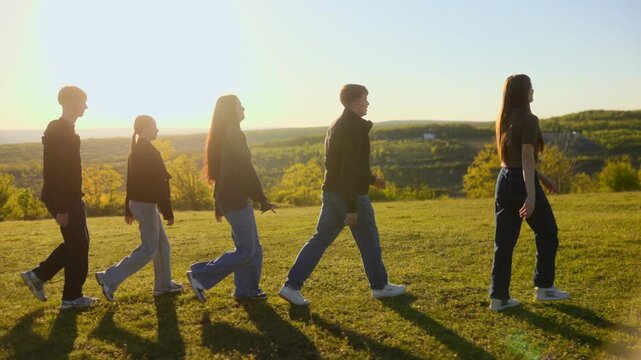 Side view of five students walking in a sequence on a green hill