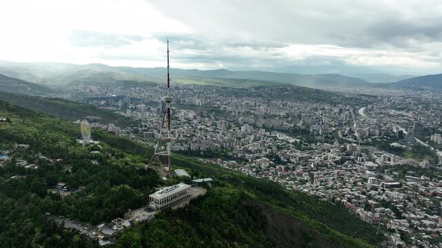 Aerial view of the Funicular Restaurant at Mtatsminda Park during sunset. Dynamic drone shot of a TV tower with Tbilisi city in the background.