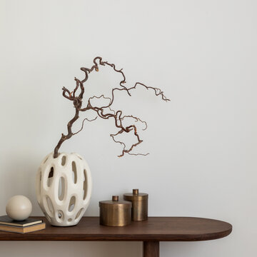 Stylish and minimalist composition on wooden design commode with copy space, dried brunch in vase, decorations and personal accessories. Template.