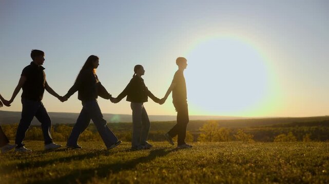 Five friends holding hands walking in silhouette across sunset