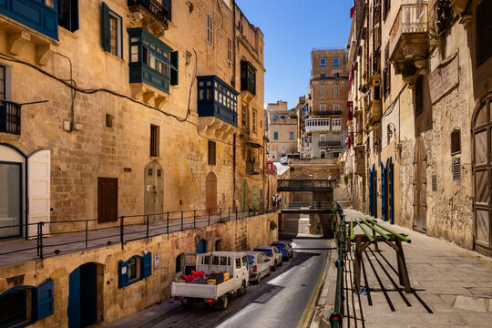 Traditional narrow street in Valletta with colorful wooden balconies and cars