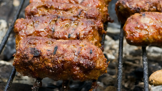Close-up of traditional Romanian mici (mititei) grilling on a charcoal barbecue. Juicy, sizzling grilled meat sausages, perfect for outdoor cooking.