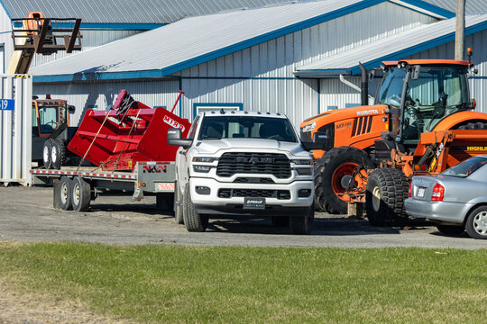 Quebec, Canada, 24 April 2026 : A white RAM pickup truck tows a red MIRB agricultural implement on a trailer, near an orange Kubota tractor.
