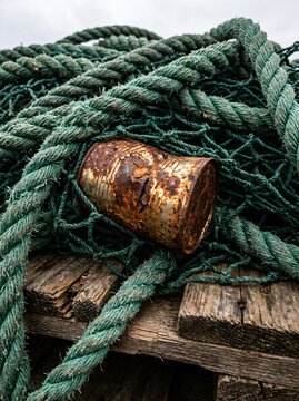 Heavily rusted tin can entangled in synthetic trawl nets on a wooden pallet, illustrating overfishing, marine resource depletion, and ocean pollution