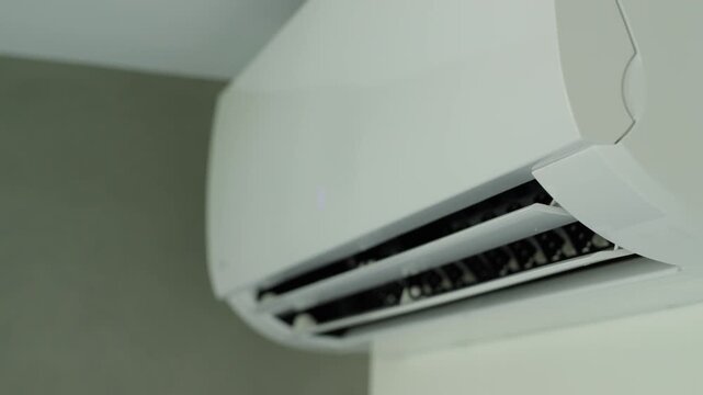 Modern wall mounted air conditioner unit opening louver blades to start cooling room.