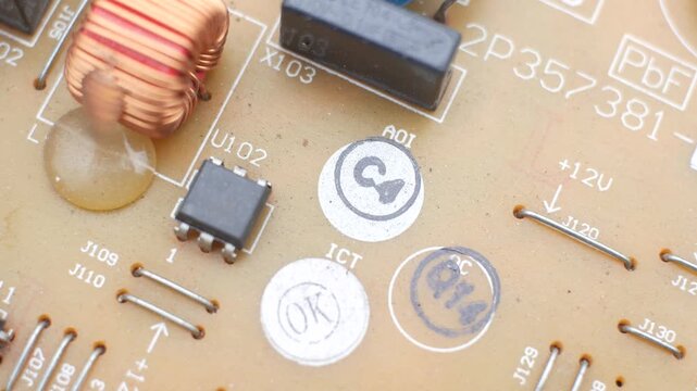 A detailed macro view of an electronic circuit board, showcasing microchips, copper coils, and various soldered components. The camera slowly pans across the complex beige PCB surface.