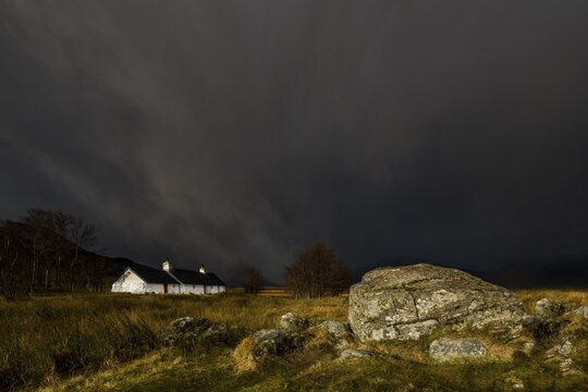 Black Rock Cottage in front of thunderstorm with Glen Coe, Rannoch Moor, west Highlands, Scotland, United Kingdom, in the background