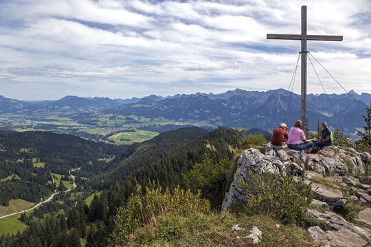 Hikers taking a break at the summit cross of the Besler with a view of the Illertal and the Allg&auml;u Alps, near Obermaiselstein, Oberallg&auml;u, Allg&auml;u, Bavaria, Germany