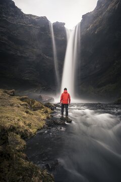 Man in red jacket in front of Kvernufoss waterfall in a gorge, dramatic atmosphere, time exposure, near Sk&oacute;gafoss, Southurland, Iceland