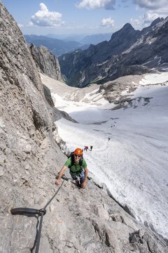 Mountaineer with helmet in a secured via ferrata, Zugspitz via ferrata, ascent to the Zugspitze, behind snowfield of the H&ouml;llentalferner and H&ouml;llental, Wetterstein range, Bavaria, Germany