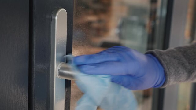 Person wearing protective blue gloves cleaning door handle with disinfectant wipe to prevent virus spread.