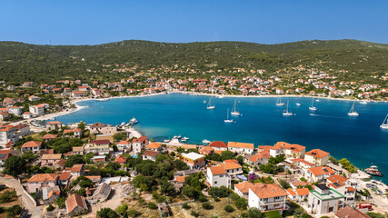 Wide aerial view of a calm coastal bay surrounded by seaside buildings and anchored yachts on the Adriatic coast of Croatia. © Tomasz