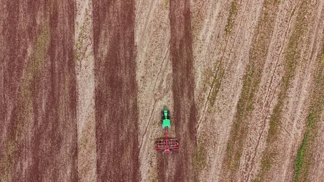 A green tractor works on a field, creating straight lines in the soil. It is late morning, and the tractor moves along the rows with care in a farming area.