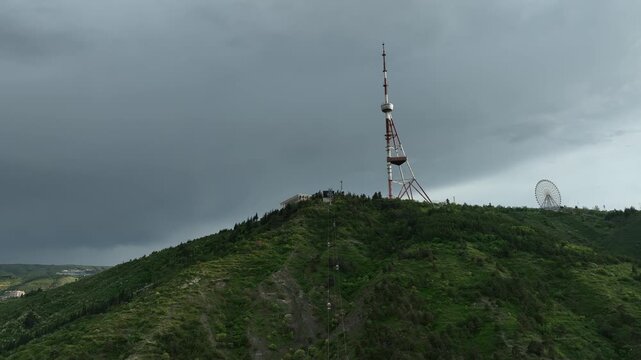 Aerial view of the Funicular Restaurant at Mtatsminda Park during sunset. Dynamic drone shot of a TV tower with Tbilisi city in the background.