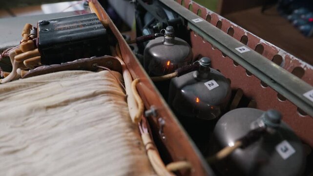 Glowing vacuum tubes operate inside a custom audio amplifier chassis alongside wiring and a cooling fan. This visualizes the concept of vintage audio engineering technology.