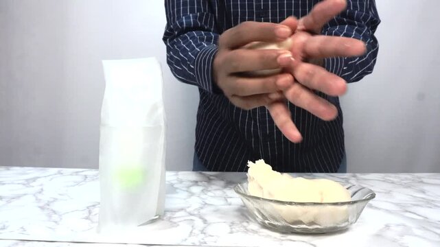 Man Rolling Dough by Hand in Kitchen for Homemade Bread or Pizza Preparation, Close-up of a man shaping and rolling soft dough by hand on a kitchen counter during homemade bread or pizza preparation. 
