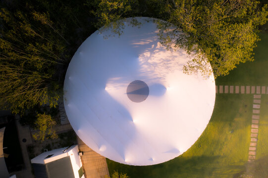 Aerial view of a large white circular marquee tent surrounded by lush green lawn and trees during golden hour Cape Town, Western Cape, South Africa.