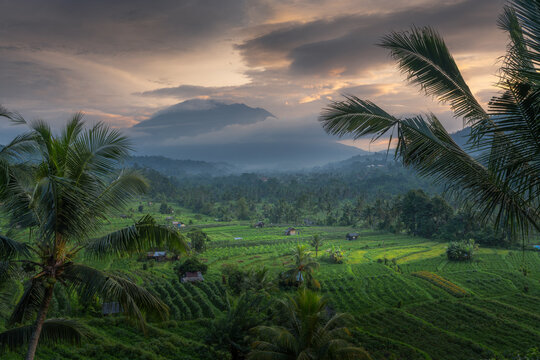 Aerial view of the Sidemen rice terraces and tropical valley with Mount Agung in the background under a dramatic sunset sky Sidemen, Bali, Indonesia.