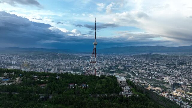 Aerial view of the Funicular Restaurant at Mtatsminda Park during sunset. Dynamic drone shot of a TV tower with Tbilisi city in the background.