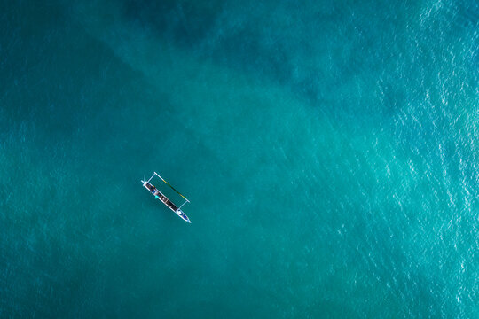 Aerial view of a traditional wooden boat floating on the turquoise ocean water with slight ripples at Tanjung Aan Beach, Kecamatan Pujut, Nusa Tenggara Barat, Indonesia.