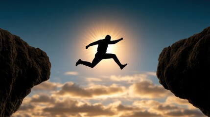 Fototapeta premium Silhouette of a person jumping across a gap between two cliffs with the sun shining behind and a cloudy sky in the background at sunset or sunrise