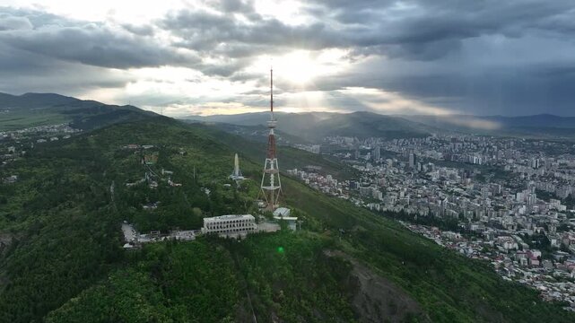 Aerial view of the Funicular Restaurant at Mtatsminda Park during sunset. Dynamic drone shot of a TV tower with Tbilisi city in the background.