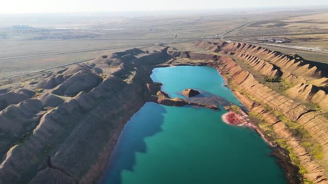 Drone pullaway showing a turquoise lake and massive red refractory clay hills with bauxite ore dumps. A technogenic landscape of abandoned quarries near Arkalyk, Kostanay region. Surreal industrial mi
