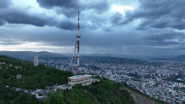 Aerial view of the Funicular Restaurant at Mtatsminda Park during sunset. Dynamic drone shot of a TV tower with Tbilisi city in the background.
