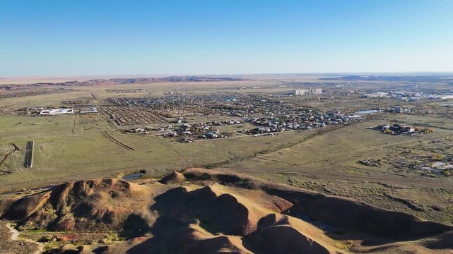Drone view of massive bauxite ore dumps and red refractory clay hills with the Arkalyk city skyline on the horizon. Industrial aluminum mining landscape in the Kostanay region, Kazakhstan. Footage cap