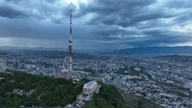 Aerial view of the Funicular Restaurant at Mtatsminda Park during sunset. Dynamic drone shot of a TV tower with Tbilisi city in the background.