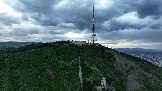 Aerial view of the Funicular Restaurant at Mtatsminda Park during sunset. Dynamic drone shot of a TV tower with Tbilisi city in the background.
