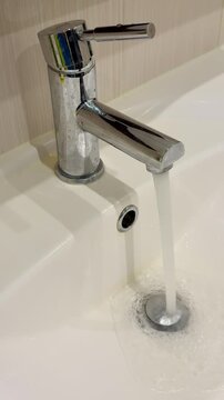 Dirty stainless faucet pouring water into unclean acrylic sink, visible mineral stains and soap scum around drain, slow steady