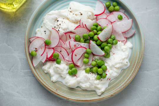 Salad with fresh radish, green peas and torn burrata cheese served on a turquoise plate, middle close-up, horizontal shot
