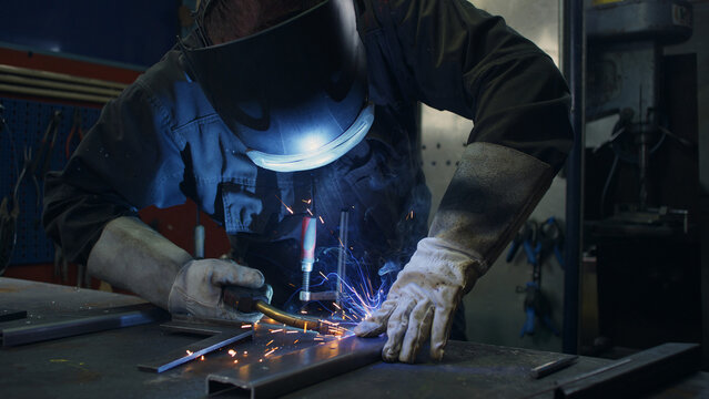 Skilled welder worker with experience in metal fabrication, using MIG welding techniques to create sparks and shape metal components.