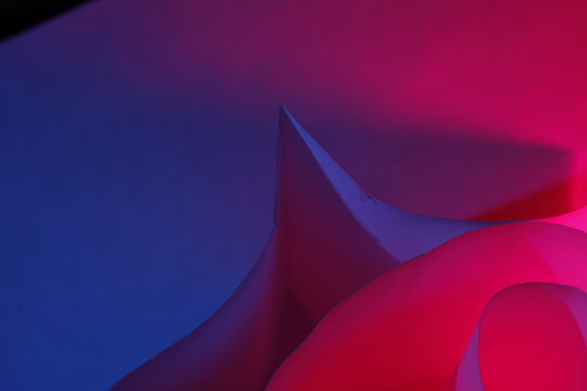 Composici&oacute;n abstracta de papel reciclado con l&iacute;neas curvas y formas fluidas iluminadas con luces ne&oacute;n en tonos azul y magenta. La escena destaca texturas artesanales y contrastes intensos.