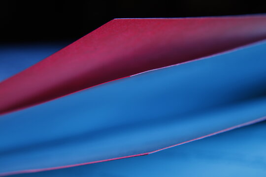 Hojas de un libro entreabiertas en tonos rojo y azul,  destaca los bordes curvos del papel y el efecto de desenfoque art&iacute;stico del fondo, creando una imagen moderna y creativa.