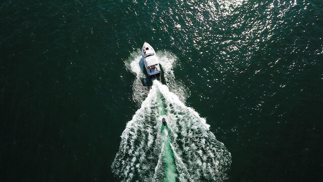 Aerial view of a white motorboat and a jet ski cruising through dark green water with white foam wakes Saint-Prex, Vaud, Switzerland.