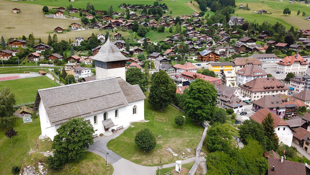 Aerial view of the Temple of Chateau-d'Oex and traditional alpine chalets nestled in a lush green valley under soft daylight Chateau-d'Oex, Vaud, Switzerland.