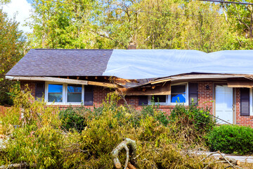 Damaged house with roof covered by tarp after storm in residential area © ungvar