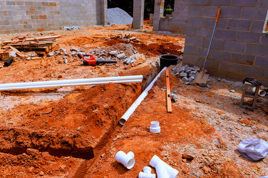 Construction site dug trench with pipes, tools on red soil landscape during waste utility system