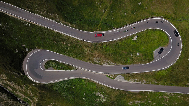 Aerial view of the winding Furka Pass mountain road with hairpin turns and cars driving through green alpine slopes in Obergoms, Valais, Switzerland.