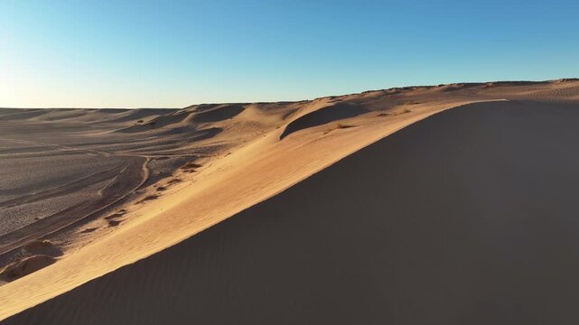 Low aerial view along sharp sand dune crest with golden sunlit slope and deep shadow contrast, Sahara desert Morocco