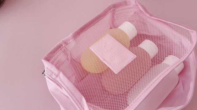 Woman closing a pink travel cosmetic bag with pastel toiletry bottles, perfect for organizing beauty products and skincare essentials for vacation or a trip