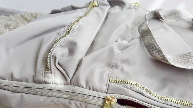 Close up of a stylish grey nylon travel duffel bag with gold zippers being opened to reveal a pink mesh packing cube, preparing for a journey or packing for vacation