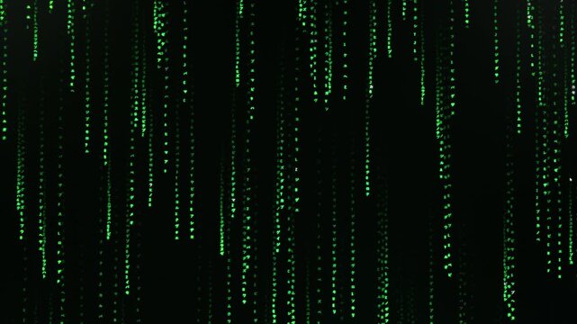Green digital characters and symbols cascade down a black screen in a matrix style rain. Cyber security and computer programming concept.