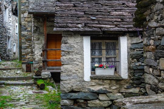 Traditional Stone House Facade with Flowers on Window in Corippo Village | Ancient Rural Architecture with Wooden Door, Slate Roof and Cobblestone Street | Swiss Alpine