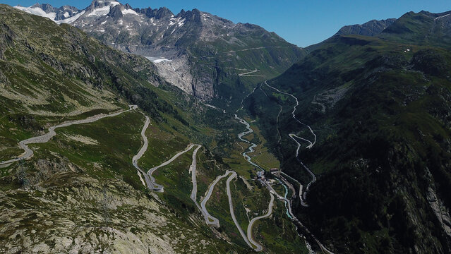 Aerial view of Grimsel Pass featuring winding serpentine roads through rugged mountain peaks and a distant glacier Obergoms, Valais, Switzerland.