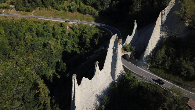 Aerial view of Pyramides d'Euseigne, unique earth pyramids with a road tunnel passing through them, surrounded by lush green forest Heremence, Valais, Switzerland.