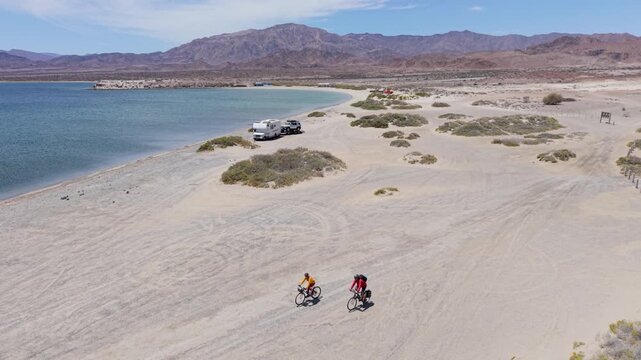 A mature man and woman bike along the sea shore near La Gringa in Bahia De Los Angeles. They explore the sandy landscape and water.